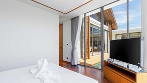 Une chambre d’hôtel moderne dotée d’un grand lit, d’un téléviseur à écran plat et d’une porte-fenêtre coulissante donnant sur un balcon.