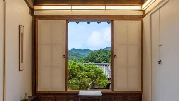 A traditional Japanese room with tatami flooring, a low table with cushions, and a view of a mountainous landscape through a sliding door. - Rakkojae Hahoe Hanok Hotel  (Andong)