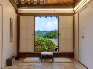 Et traditionelt japansk rum med tatamimåtter, et lavt bord med puder og udsigt til et bjergrigt landskab gennem en skydedør.