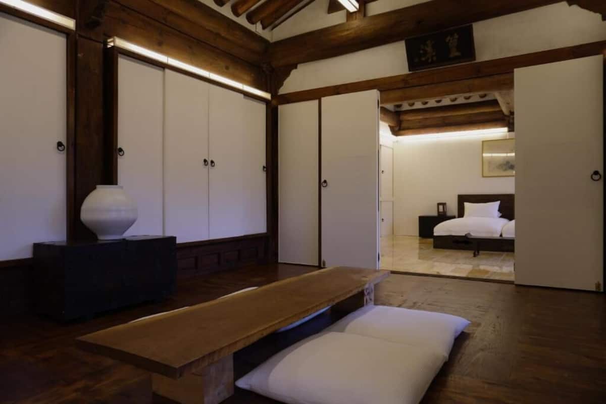 A room with wooden beams, a bed, a bench, and a large vase.