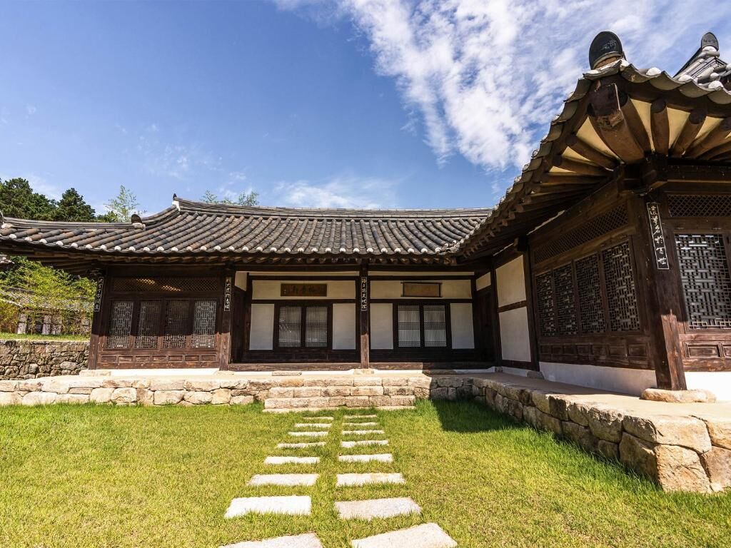 Un edificio tradicional coreano con tejado de tejas, vigas de madera y un camino de piedra que conduce a la entrada.