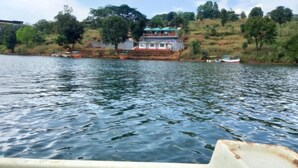 A calm lake with boats and a building on the shore. - Jalvishwa agro tourism & River camp Tapola (Satara)
