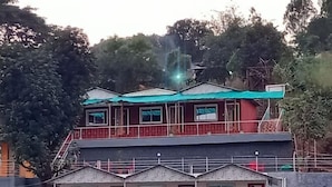 A two-story building with a balcony on the upper floor and a small attached structure with a sloped roof. - Jalvishwa agro tourism & River camp Tapola (Satara)