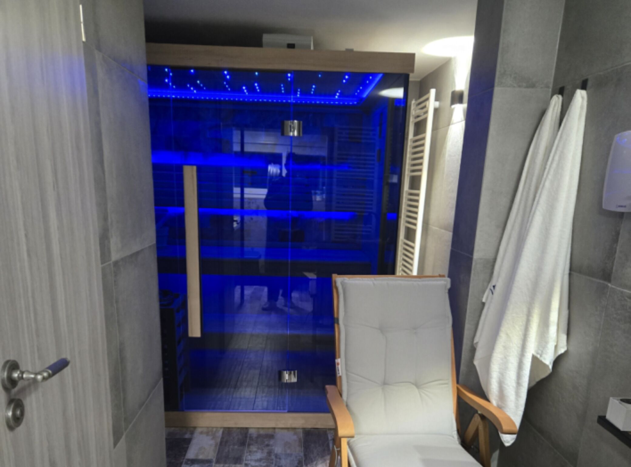 Un baño moderno con cabina de ducha de vidrio, una silla blanca y un perchero para toallas.