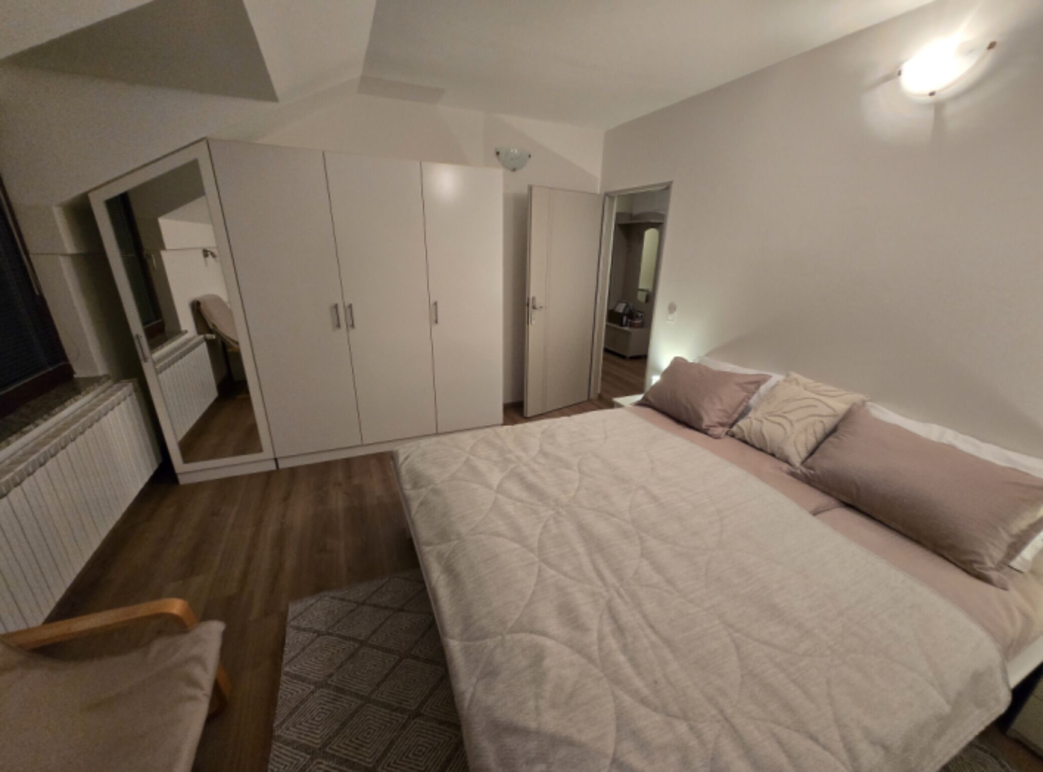 A bedroom with a bed, a wardrobe, a mirror, and a radiator.