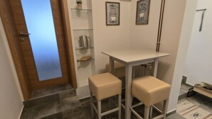 A small kitchen area with a white table and two beige stools. There is a wooden door with a frosted glass panel, a shelf with a potted plant, and two framed signs on the wall. - Villa Bella Vista (Ivanec)