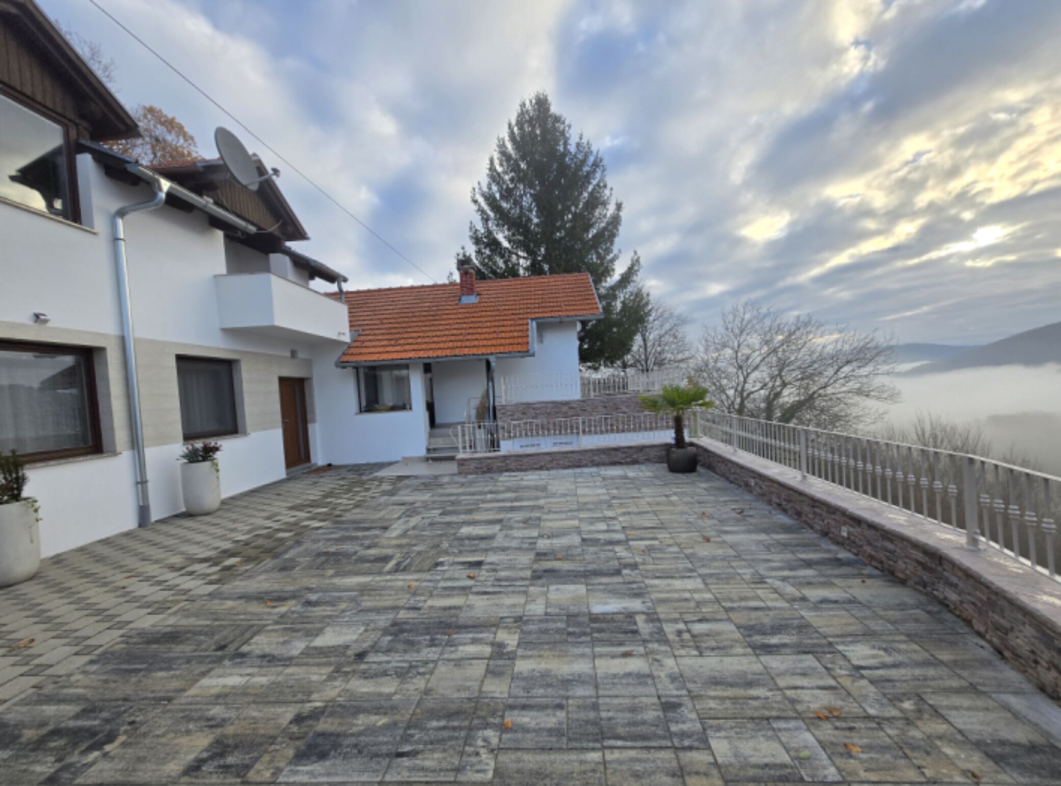 A modern house with a tiled patio, a small garden, and a view of the mountains.