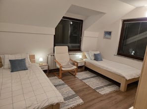 A bedroom with two beds, a chair, a radiator, and two windows with blinds. - Villa Bella Vista (Ivanec)