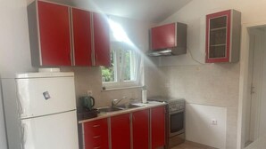 A compact kitchen with red cabinets, a white refrigerator, a stove, and a window above the sink. - Family House Kurtin by Brankica (Preko)