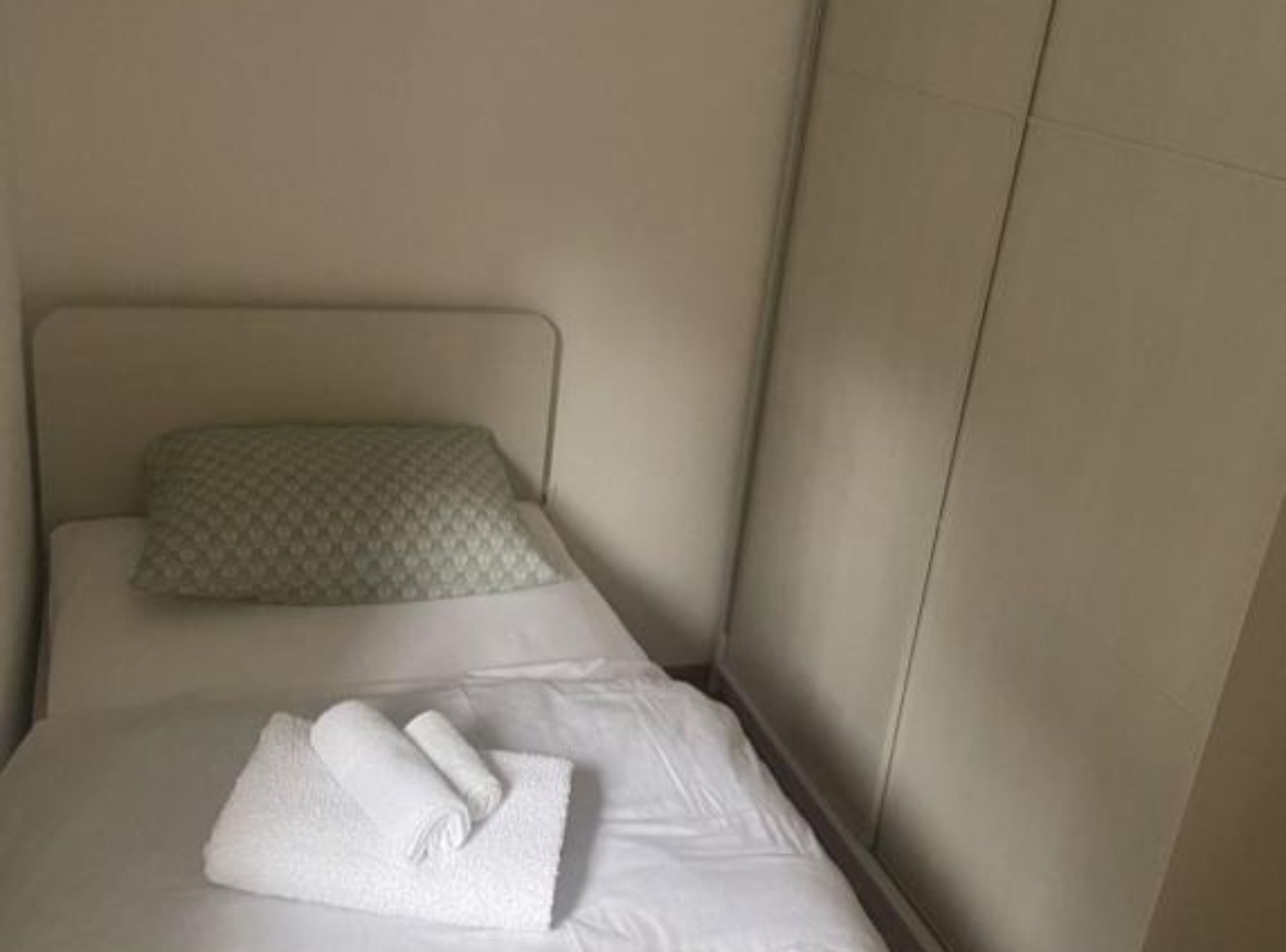 Ein Einzelbett mit Kopfteil, einem Kissen und einem zusammengerollten Handtuch.
