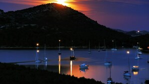 Uma marina com barcos ancorados em águas calmas, emoldurada por uma paisagem ondulante ao pôr do sol.