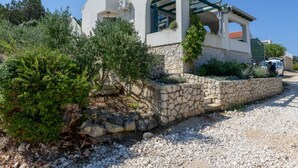Uma casa moderna com um muro de pedra, uma área externa coberta e um caminho de acesso de cascalho.