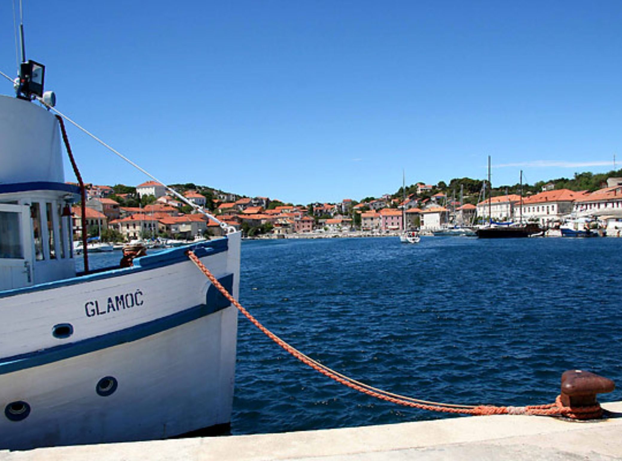 A boat named 'GLAMOC' docked at a harbor with buildings in the background.