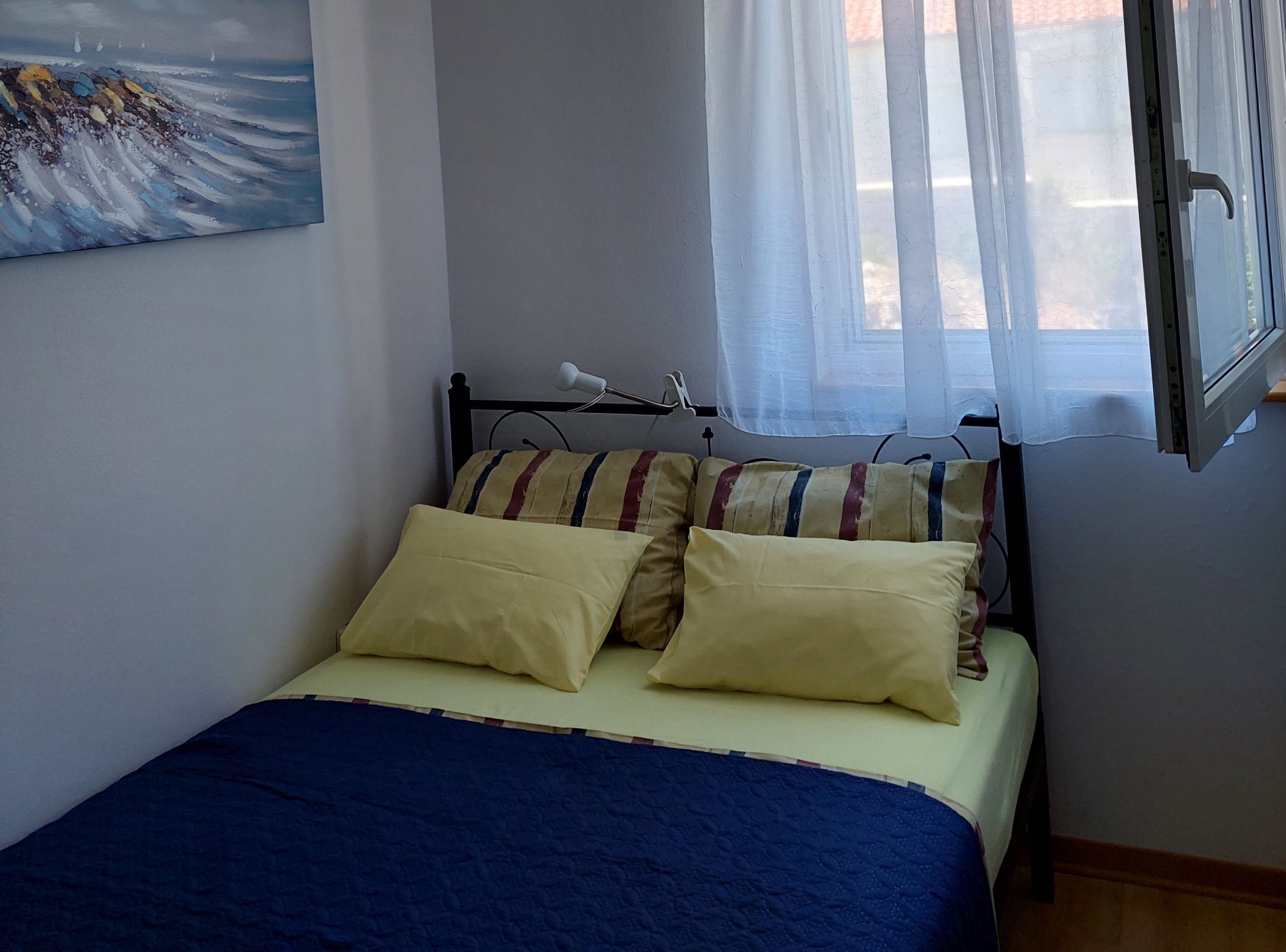 Un llit amb dos almoinos, una làmpada de nit i una finestra amb cortines transparents.