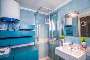 Une salle de bain moderne avec une douche à parois de verre, un lavabo blanc et des meubles de rangement bleus.