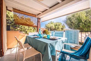 Un espace de restauration en plein air avec une table dressée pour deux personnes, des chaises et une vue sur des arbres et un bâtiment en arrière-plan.