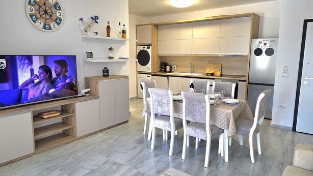 A modern kitchen with a built-in oven, a refrigerator, and a dining area with a table and chairs. - Holiday Apartment in Golem 070 (Golem)