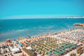 A beach with numerous umbrellas and sun loungers, a clear blue sea, and a distant cityscape. - Holiday Apartment in Golem 070 (Golem)
