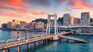 Eine moderne Brücke mit Fußgängerweg über Wasser, umgeben von städtischen Gebäuden.