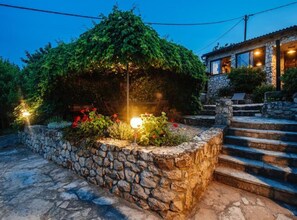 Un muro de piedra con escalones que conducen a un edificio de fachada de piedra y un jardín con flores rojas y un farol.