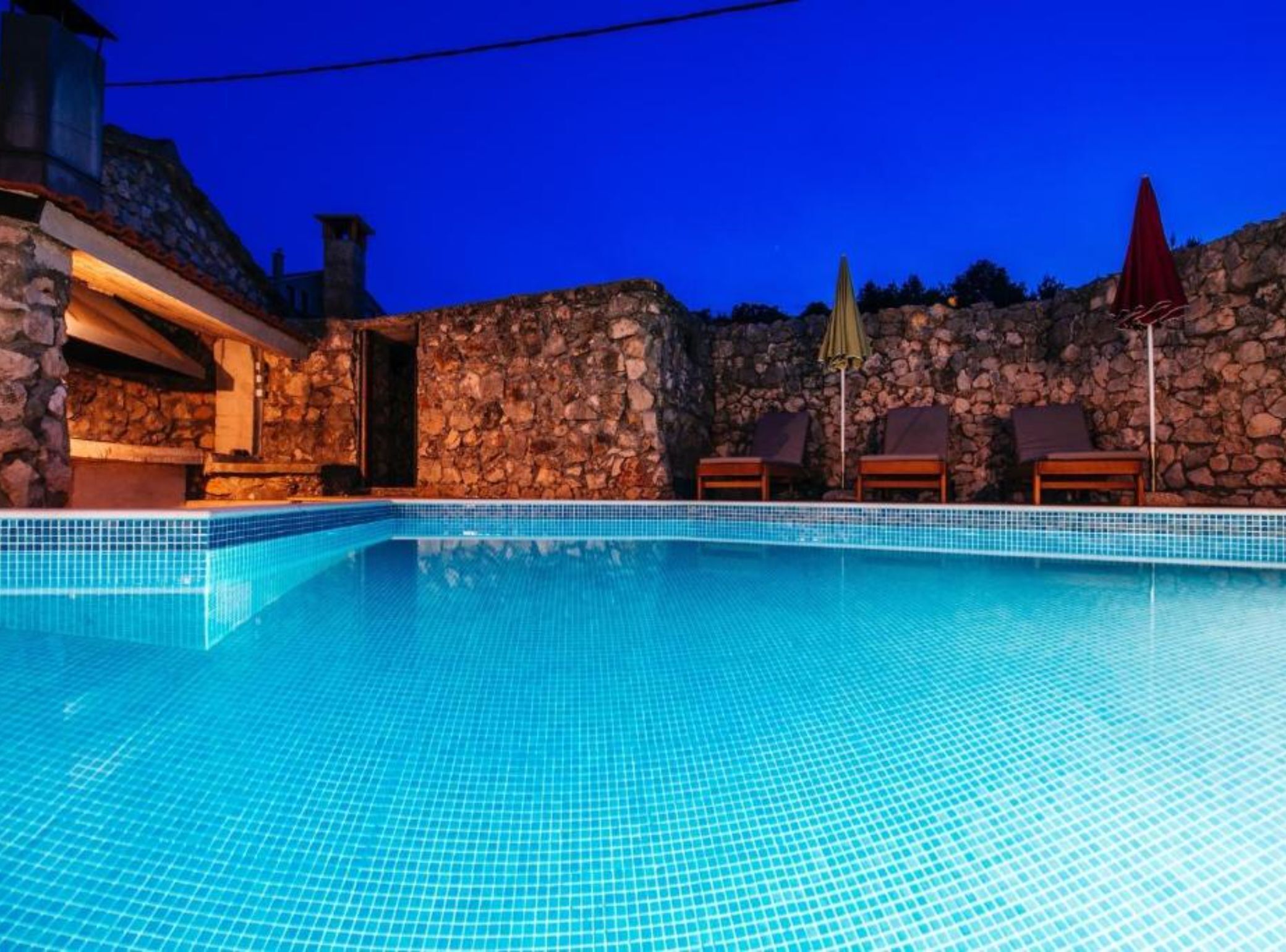 A swimming pool with stone walls and lounge chairs.
