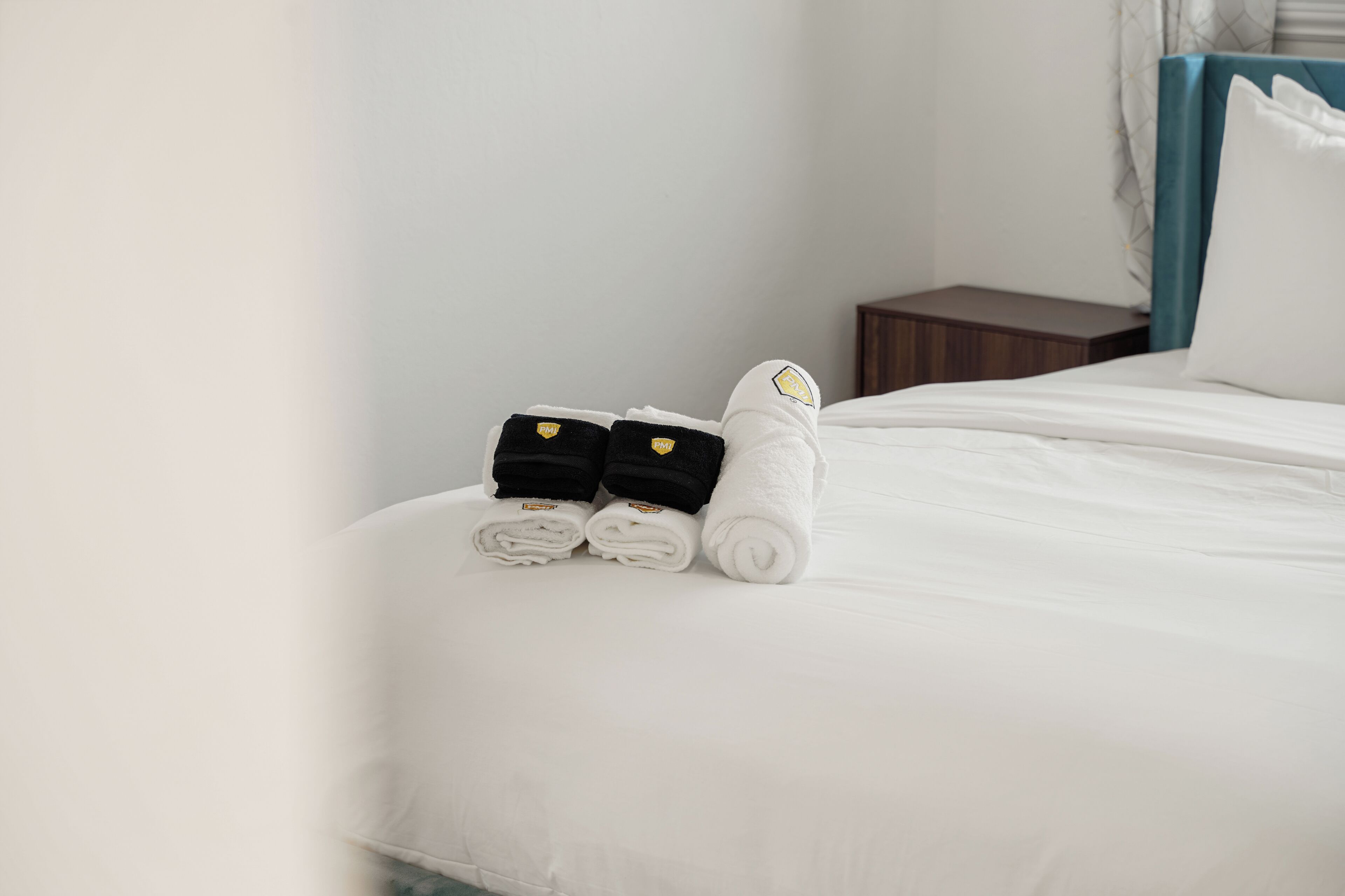 A neatly made bed with white and black towels and a small black bag on the side.