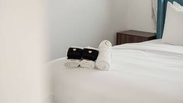 A neatly made bed with white and black towels and a small black bag on the side.
