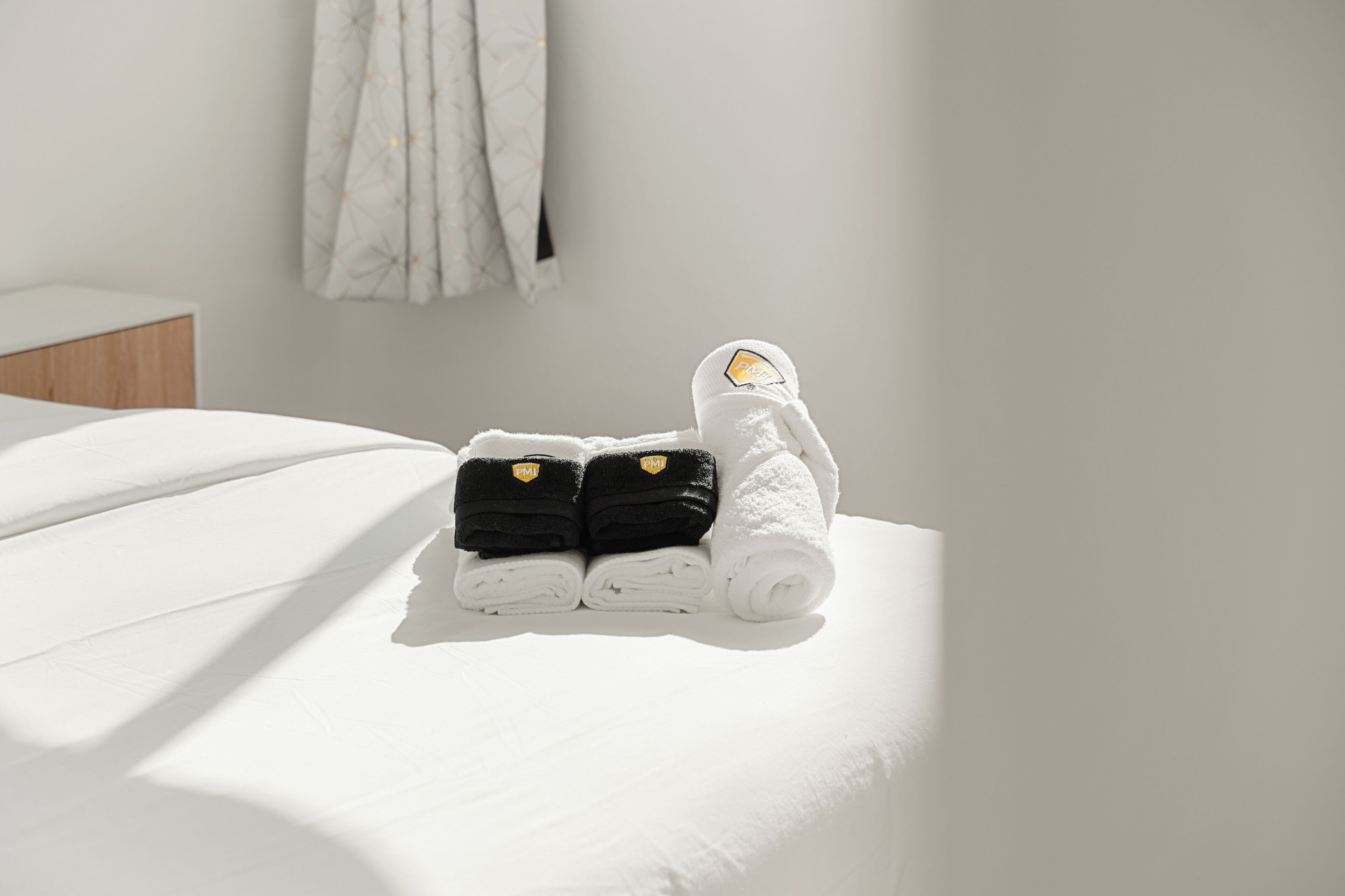 A neatly made bed with folded towels and a rolled-up towel on a white bedspread.