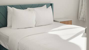 A neatly made bed with white linens and pillows, a teal upholstered headboard, and a small bedside table with a wooden nightstand.