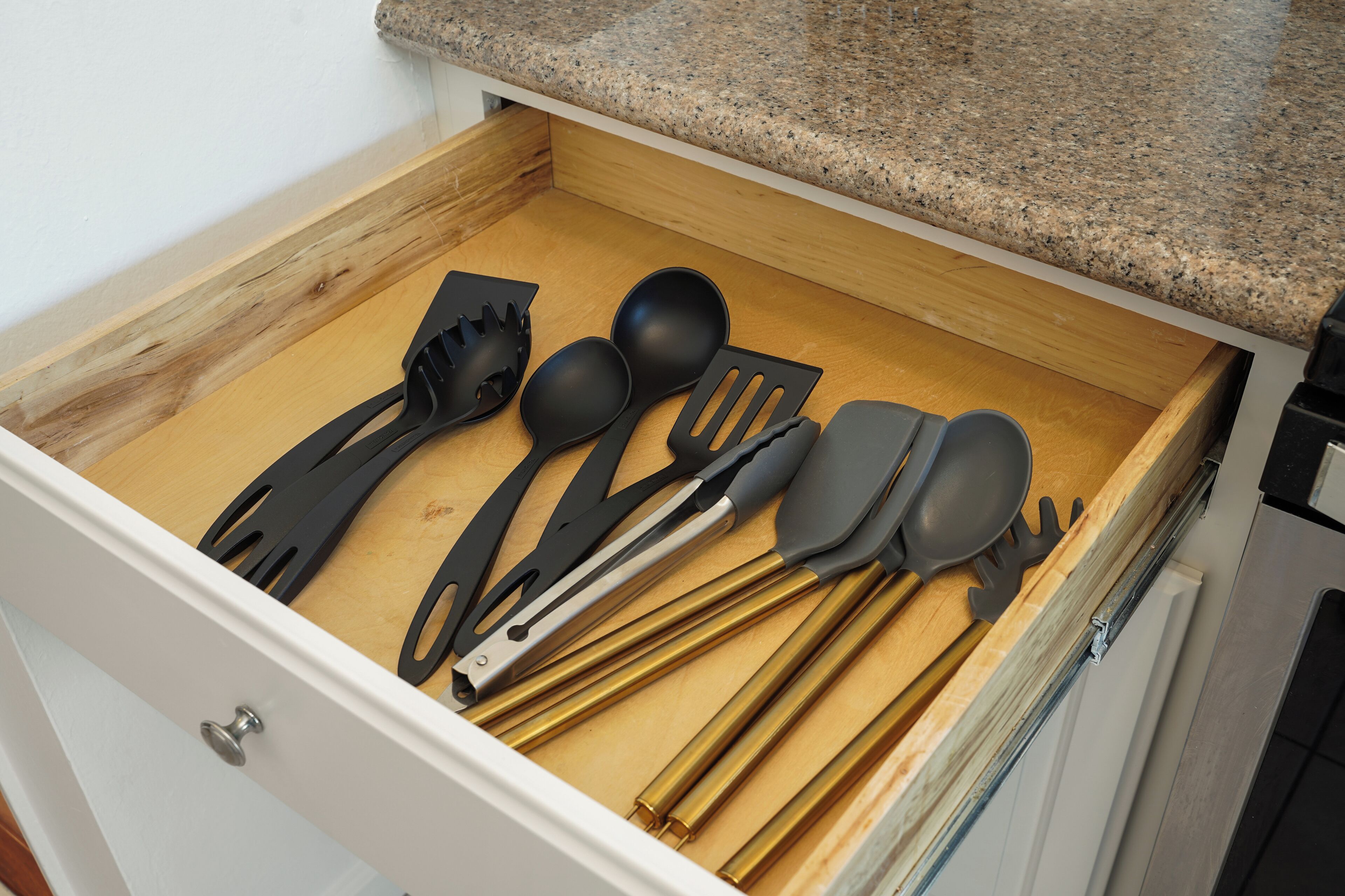 Uma gaveta com utensílios de cozinha, incluindo espátula, colher e concha.