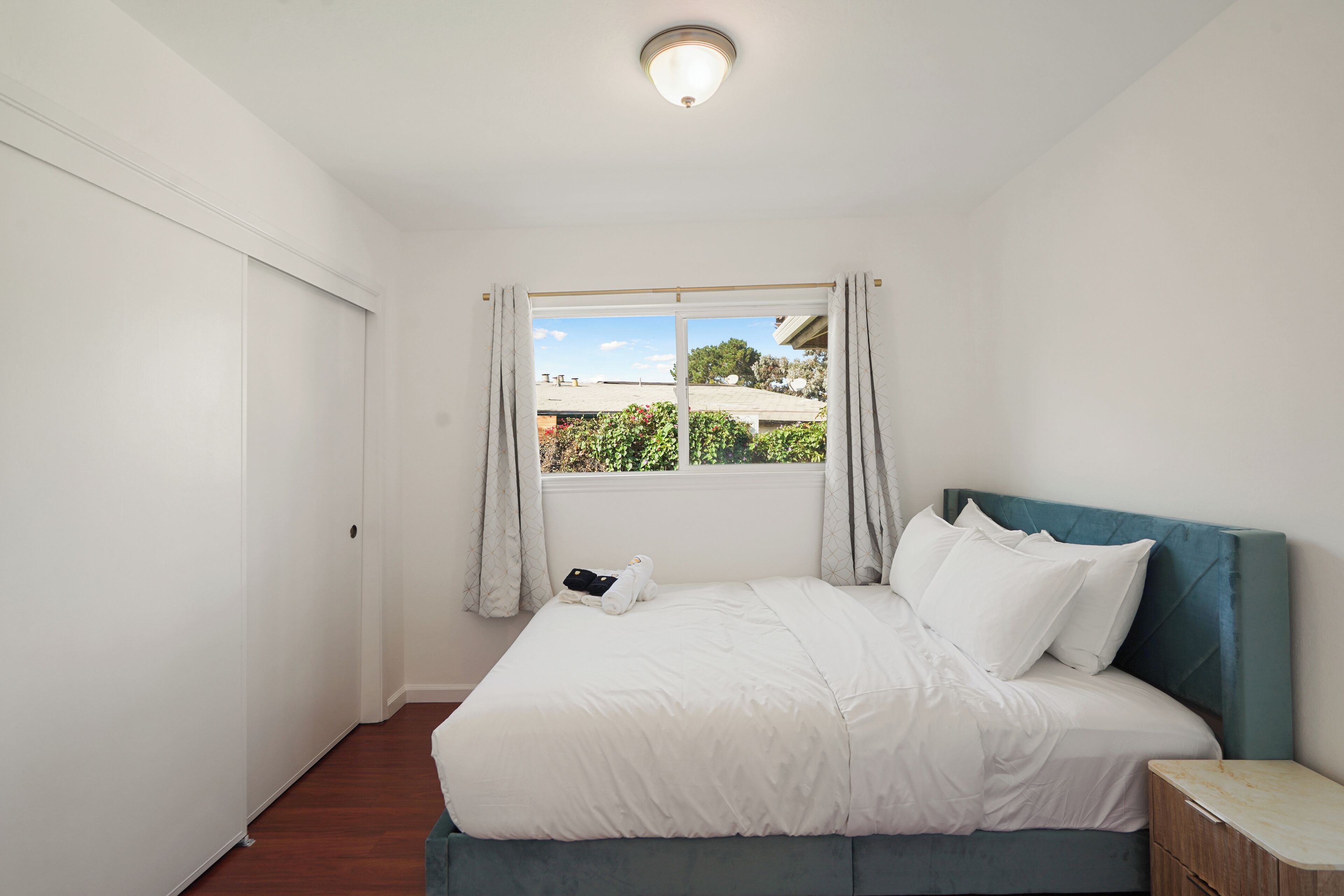 A bedroom with a bed, a window with curtains, a bedside table, and a ceiling light.