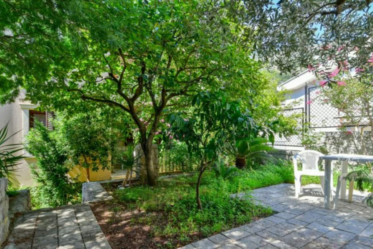 A paved patio with a small garden area, a white plastic chair, and a yellow wall in the background.