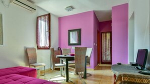 Une pièce avec un mur rose, une table à manger avec des chaises, un canapé et un téléviseur.