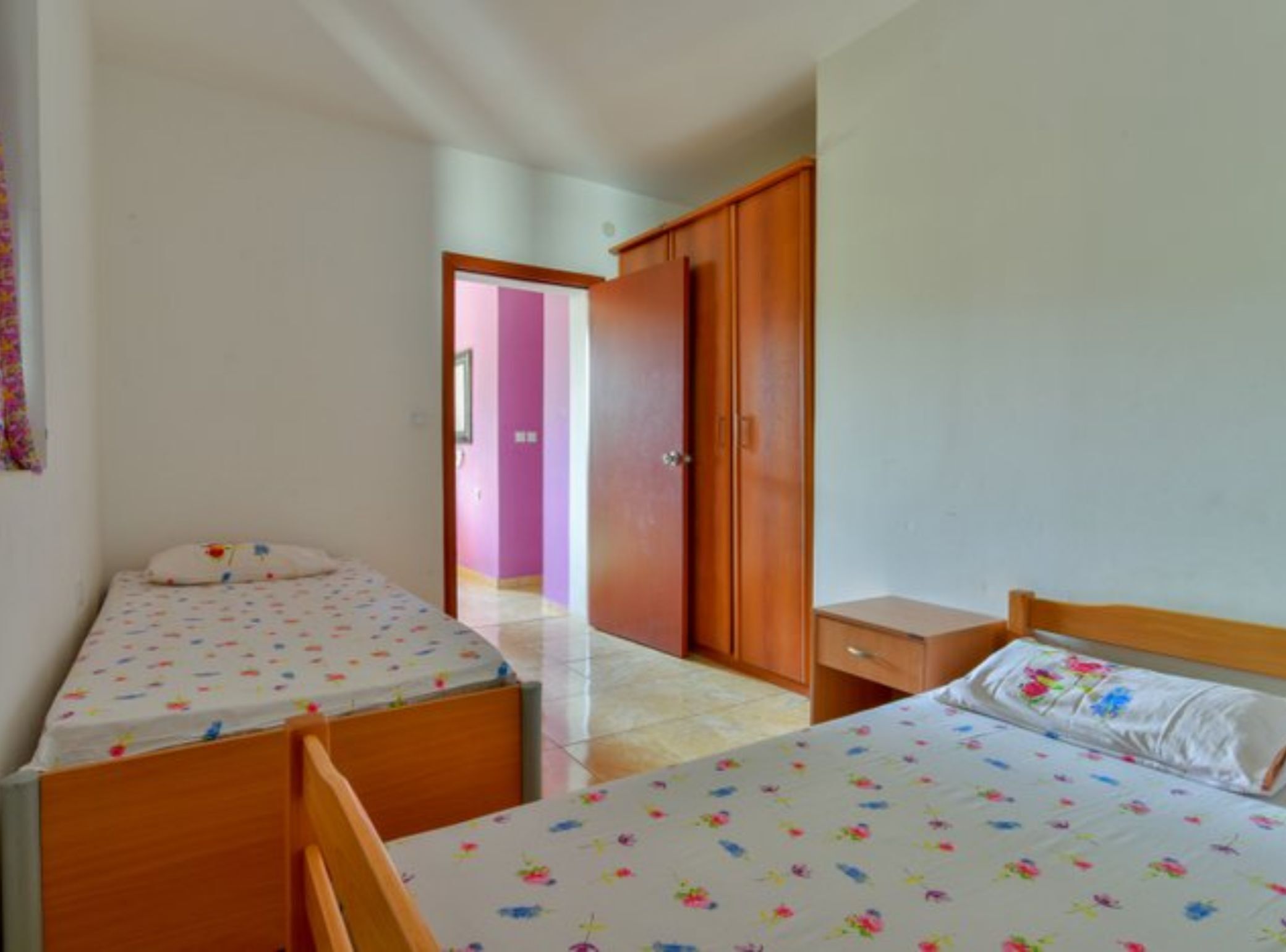 A bedroom with two single beds, a wooden wardrobe, and a small bedside table.