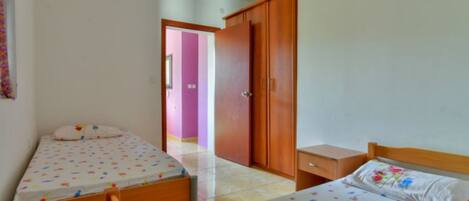 A bedroom with two single beds, a wooden wardrobe, and a small bedside table.