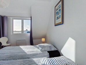 A bedroom with a bed, a chair, a window with curtains, a lamp, and a framed picture on the wall. - Ker Soizik by Interhome (Locquirec)