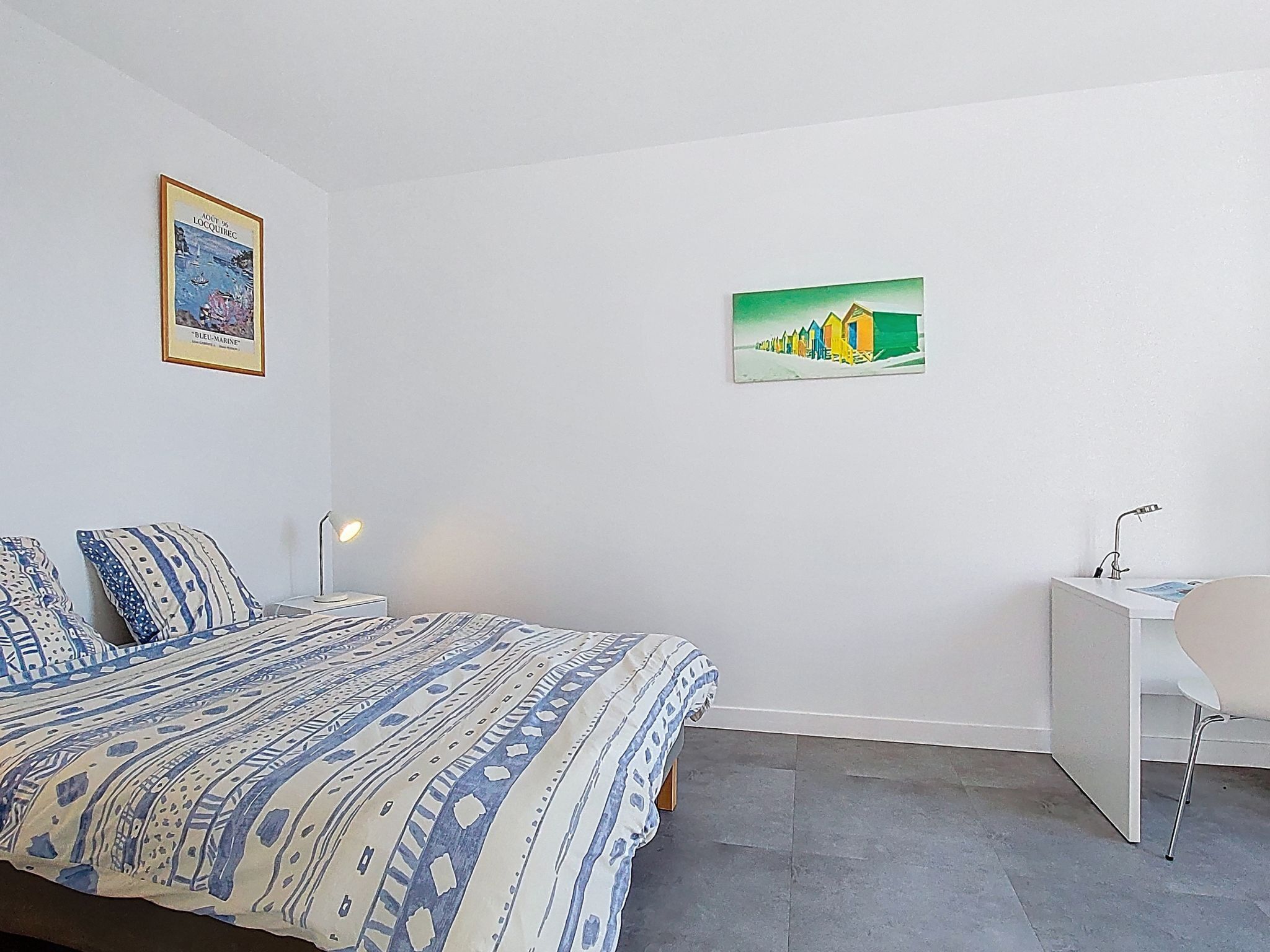 A bedroom with a bed, a desk, a chair, and two wall-mounted paintings.