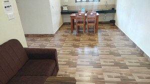 Un salon avec un canapé marron, une table basse en bois et un parquet en bois disposé en motif chevrons. On aperçoit à l’arrière-plan un coin repas avec une table et des chaises.