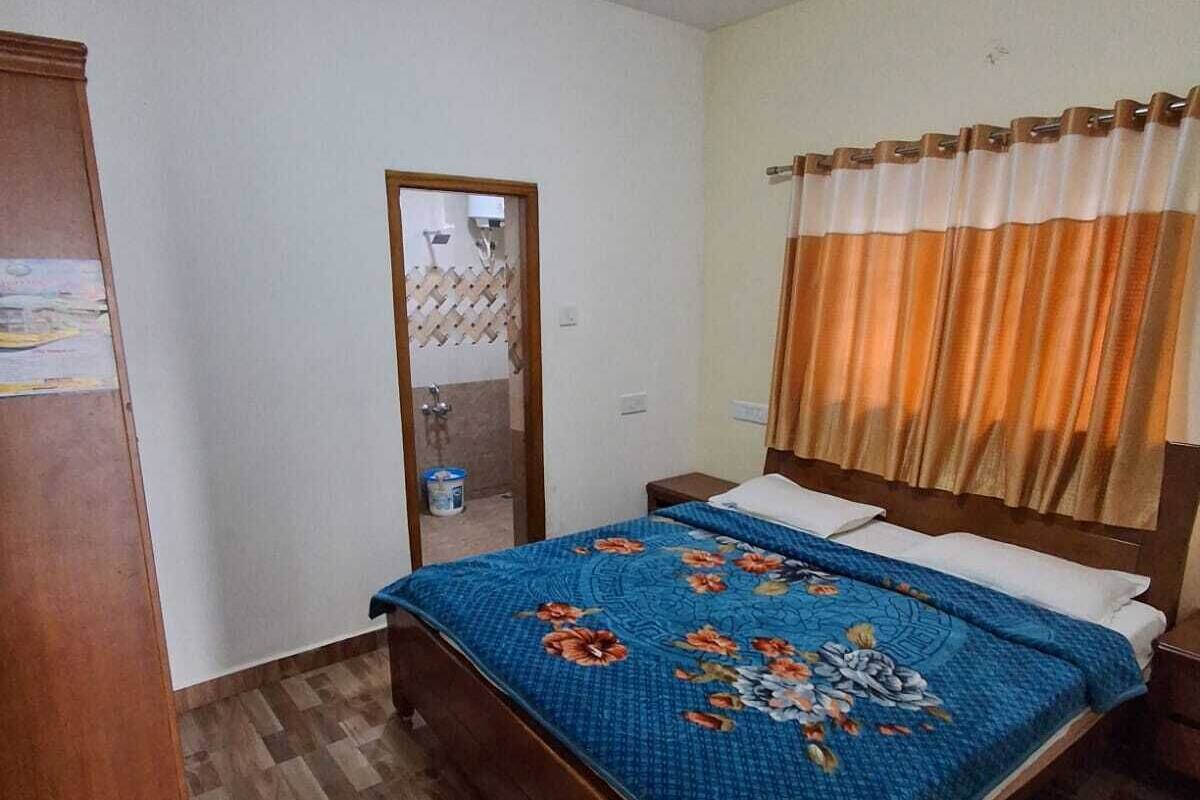 Ein Schlafzimmer mit einem hölzernen Bett, einem Kleiderschrank, einem Spiegel, einem Fenster mit Vorhängen und einem Fliesenboden.