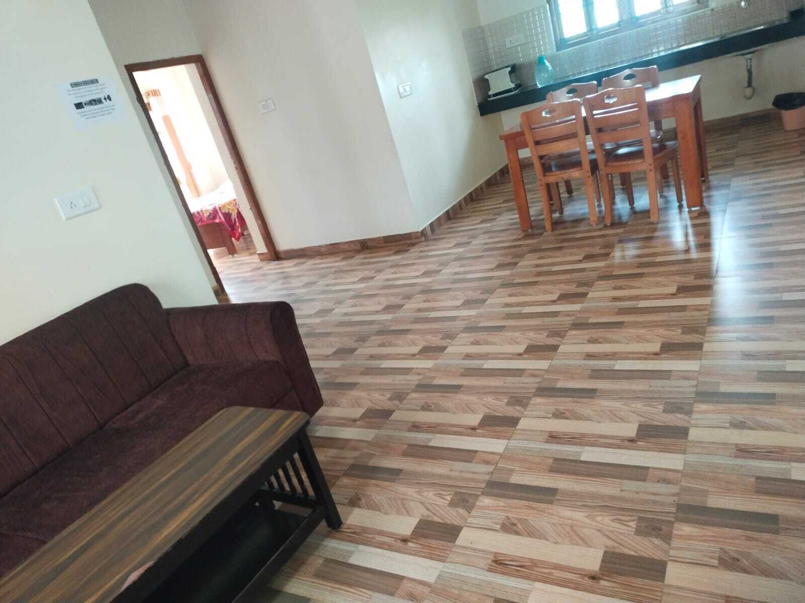 A room with a wooden herringbone floor, a brown sofa, and a dining area with wooden chairs and a table.