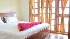 Un lit avec du linge de lit blanc et une couverture rose, une tête de lit en bois et une fenêtre avec des rideaux.