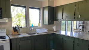 Una cocina con armarios verde oscuro, una estufa blanca y una ventana con vistas a la vegetación.