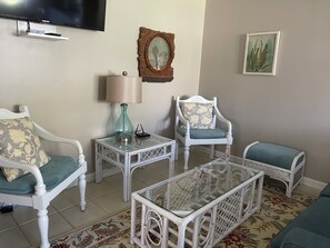 A living room with white wicker furniture, a glass coffee table, a lamp, and a television mounted on the wall. - THE SUITE:  Charming 3 bedroom In the Heart of Grace Bay!! (Grace Bay)