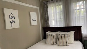 Un dormitorio con cama, dos letreros en la pared y una ventana con cortinas translúcidas.