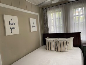 A bedroom with a bed, two wall-mounted signs, and a window with sheer curtains. - THE SUITE:  Charming 3 bedroom In the Heart of Grace Bay!! (Grace Bay)