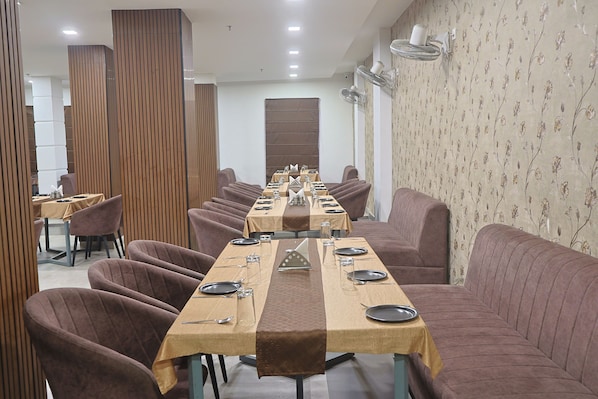 A dining area with a long table set for a meal, surrounded by cushioned seating. - Pacific Inn Paonta Sahib (Paonta Sahib)