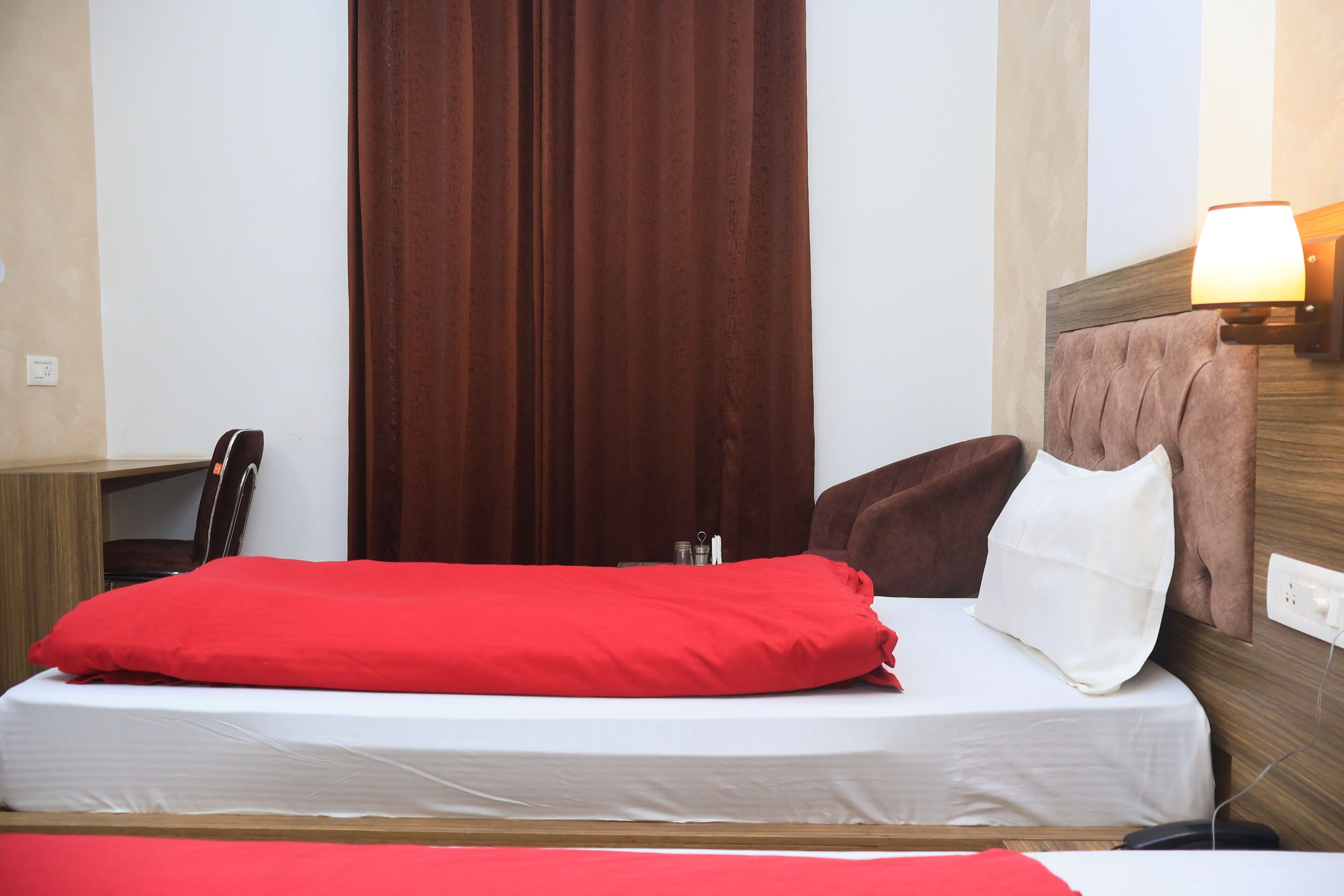 A hotel room with a bed, a desk, a lamp, and a curtain.