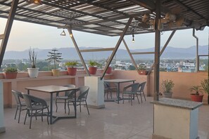 A rooftop terrace with tables and chairs, potted plants, and a view of distant mountains. - Pacific Inn Paonta Sahib (Paonta Sahib)