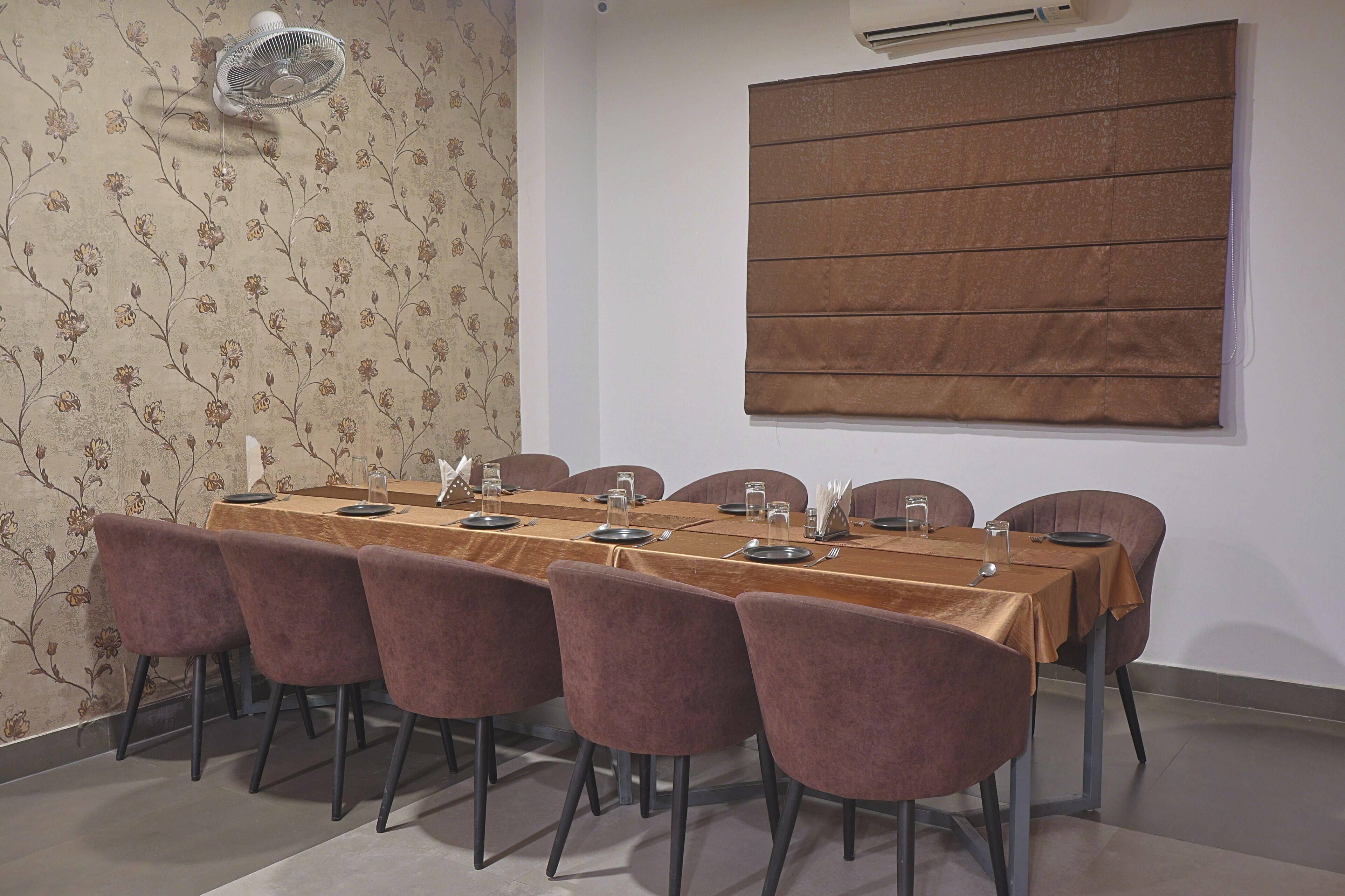Une salle de conférence avec une longue table, six chaises et une grande fenêtre équipée de stores.