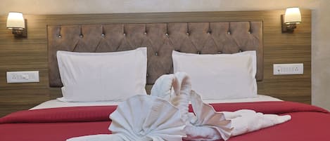 A hotel room with a tufted headboard, two white pillows, a red bedspread, and two wall-mounted lamps.